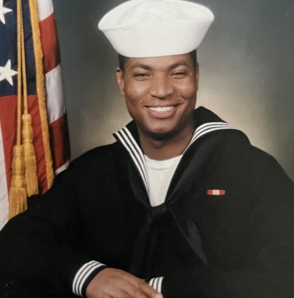 Anton Brogden in United States Navy dress uniform, with the American flag behind him.