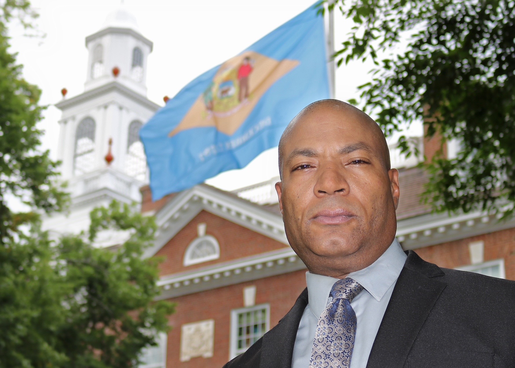 Anton Brogden outside the Old State House in Dover, Delaware, with the Delaware state flag flying behind him.