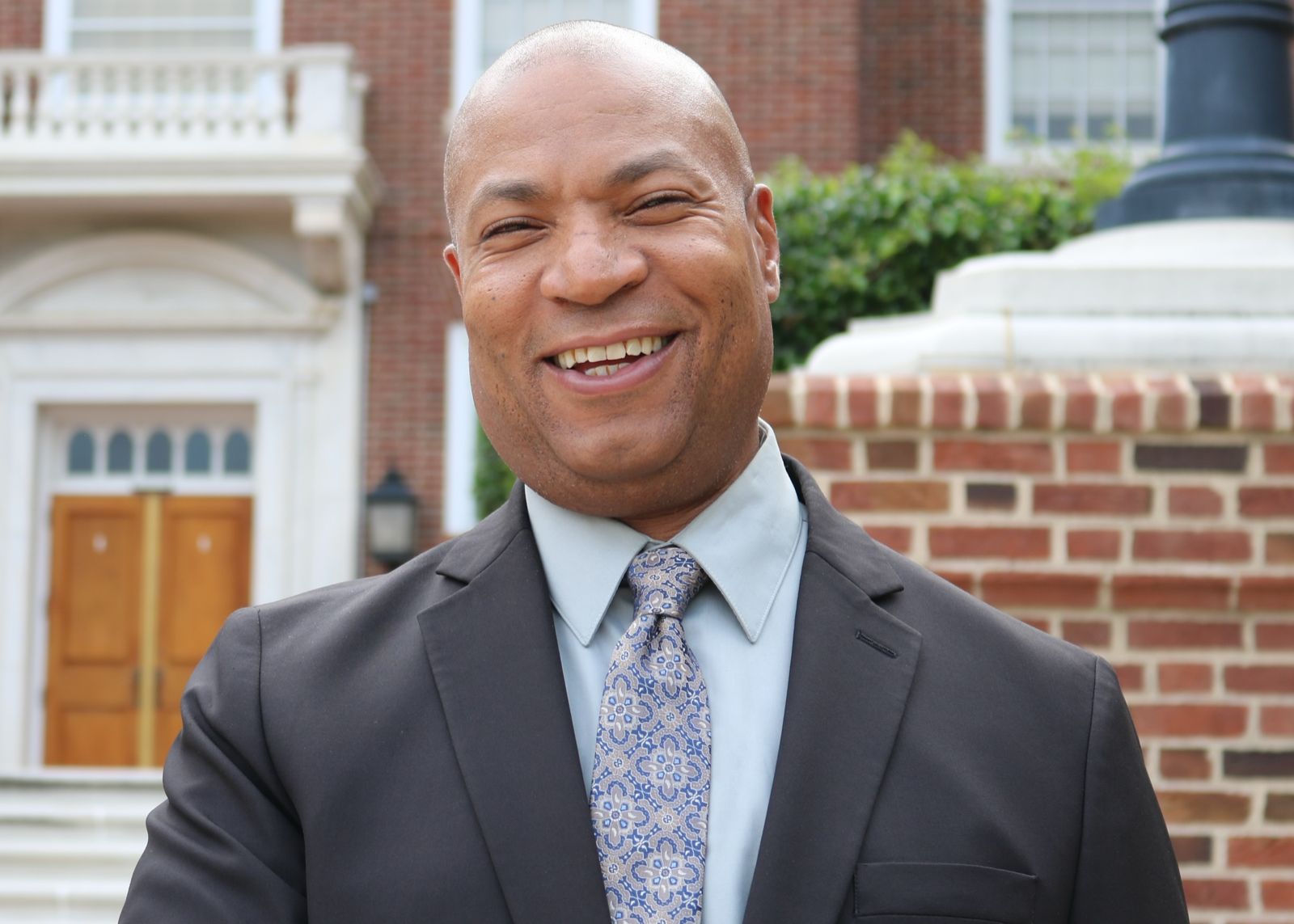 Anton Brogden smiling outside a brick public building with a white-columned doorway in Dover, Delaware.